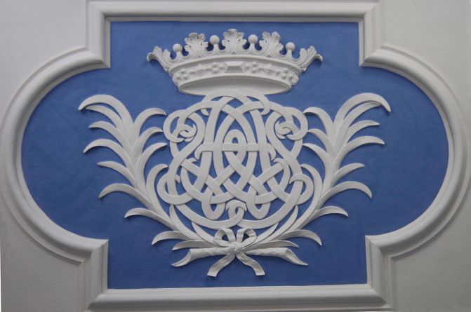 Loftdekoration fra Grevindens Kammer, hvor Christen Scheel og Augusta Winterfeldts dobbelt-monogram er afbilledet. Bogstaverne CSAW snor sig ind i hinanden og over dem er værket prydet med den ni-takkede grevekrone.